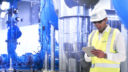 Person in hard hat in front of HVAC equipment, reviewing diagnostics on tablet